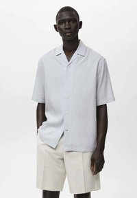 Lys blå kortærmet skjorte med knaplukning fortil og spids krave, parret med beige shorts. Glat tekstur, afslappet design.