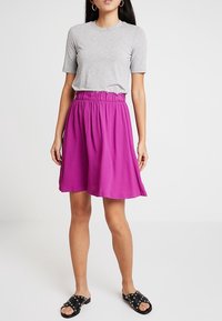 Lila knälång kjol med elastisk midja, i kombination med en åtsittande grå t-shirt. Svarta sandlettor med nitar fulländar outfiten.