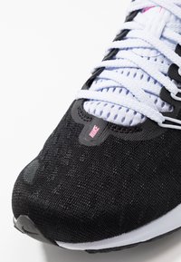 Sneaker Nike nera con upper texture, lacci bianchi e logo rosa. Il design include pannelli in mesh traspirante e una suola curva.