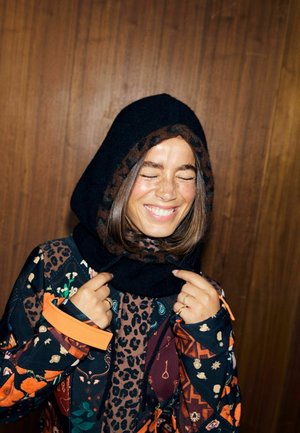 Sort og brun mønstret hættejakke med leopardprintstof. Båret over en farverig, mønstret jakke med orange og mørke motiver.