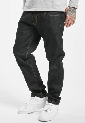 Black denim jeans with contrasting orange stitching, five pockets, a straight fit, and styled with white sneakers for a casual look.