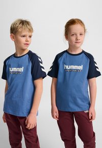 Blå och mörkblå kortärmade t-shirts med en stor "hummel SPORTSWEAR"-logotyp och vita chevron-accenter på ärmarna.