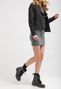 Veste de motard en simili-cuir noir avec épaules côtelées, associée à une robe grise à rayures et des bottes de combat noires brillantes avec lacets et semelles épaisses.