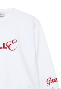T-shirt bianco a maniche lunghe con ricami rossi e argento. Tra i testi notevoli ci sono "GAE!" e "ELLE" con motivi decorativi vicino ai bordi.