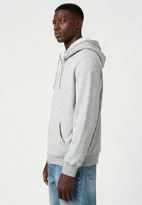 Felpa grigia con cappuccio foderato in morbido pelo crema, tasca a marsupio e polsini a coste, indossata con jeans in denim azzurri chiari.