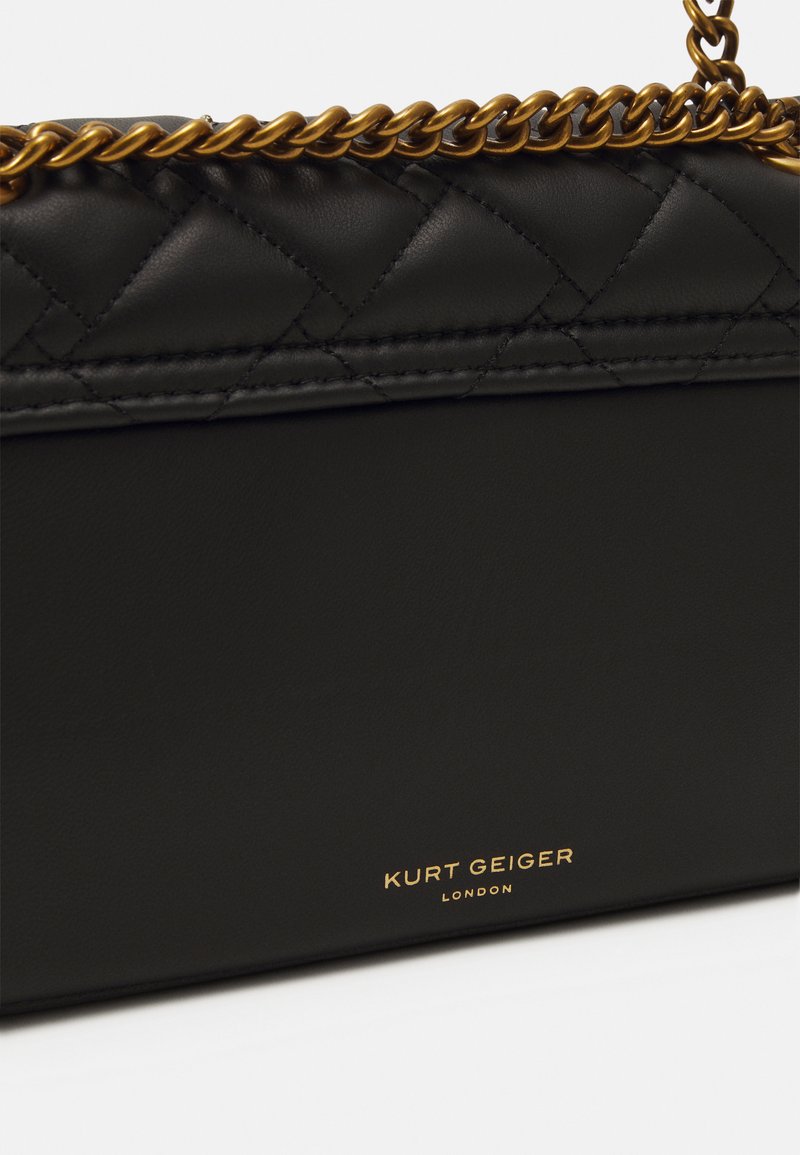 Borsa in pelle nera di Kurt Geiger con cuciture trapuntate e tracolla in oro, vista ravvicinata angolata che mostra il logo del marchio.