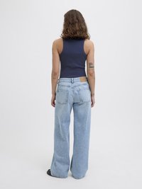 Marineblå ribbet tanktopp kombinert med lyseblå videjeans. Jeansene har en brun lærpatch på baksiden av midjen og klassisk søm.