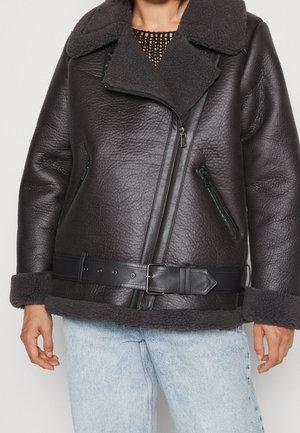 Zwarte leren jas met een schapenwol kraag en manchetten, met een ceintuurlijn en meerdere ritssluitingen. Gestructureerd oppervlak met een modern ontwerp.