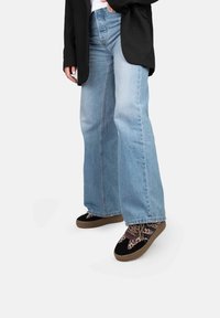 Jeans évasés bleu clair avec une finition délavée, associés à des chaussures noires à motifs avec des semelles et des lacets marron. Veste noire en dessus.