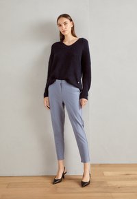 Marineblauwe oversized gebreide trui met een v-hals, gecombineerd met lichtblauwe op maat gemaakte broeken. Zwarte slingback schoenen met hakken maken de outfit compleet.
