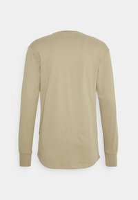 Camicia beige a maniche lunghe con polsini a coste, vista dal retro, con orlo arrotondato e un design semplice e classic.