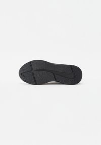 Svart sneakersåle med en strukturert overflate, med et bølgemønster og en sentral spor for fleksibilitet. Detaljer inkluderer en hevet logo.