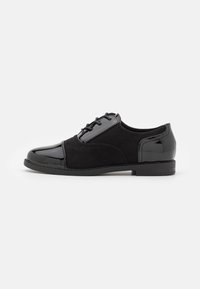 Chaussures noires à lacets combinant cuir verni et daim, avec un bout arrondi et un low heel plat.