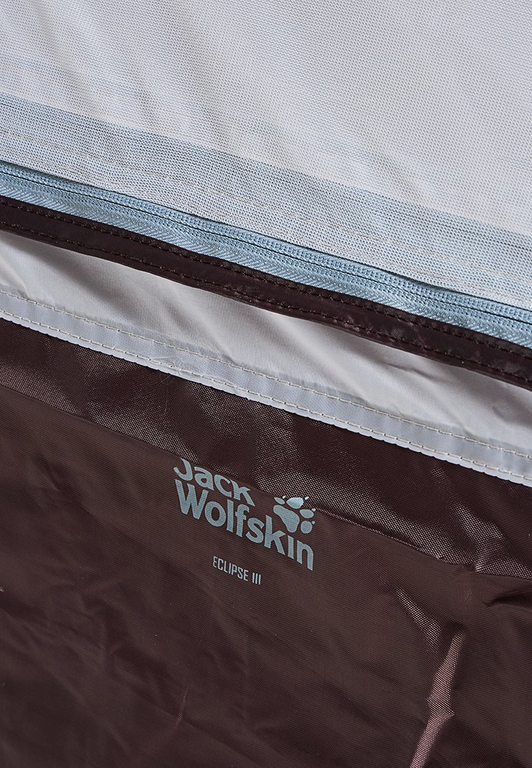 Materiał namiotu Jack Wolfskin ma bordowy dolny segment i jasnoszary górny segment z niebieskim zamkiem. Widoczne logo i nazwa modelu.