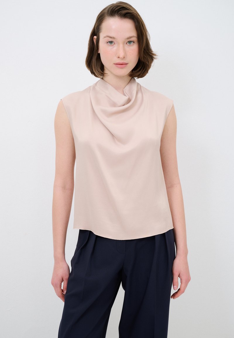 Top senza maniche di colore crema con scollo drappeggiato, texture morbida e vestibilità ampia, abbinato a pantaloni larghi blu scuro.