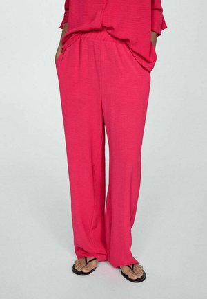 Lösa rosa byxor i lätt material, med elastiskt midjeband och sidofickor, parat med svarta flip-flops.
