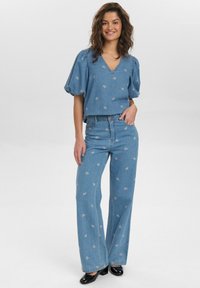 Lichtblauw denimtop met pofmouwen, V-hals en bloemborduursel, gecombineerd met bijpassende flare jeans. Zwarte hakken maken de outfit compleet.