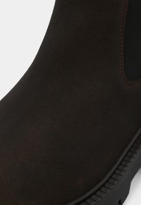 Botte de cheville en suede marron avec une finition lisse, panneau latéral élastique, coutures renforcées et semelle en caoutchouc résistante.