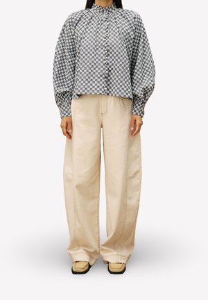 Persoon draagt een geruite blouse met lange mouwen en knopen, met pofmouwen en brede beige broek met schoenen met een vierkante neus.