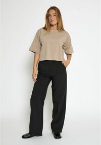 Cropped beige t-shirt with short sleeves, paired with high-waisted black wide-leg trousers and glossy black shoes. Smooth fabric texture.