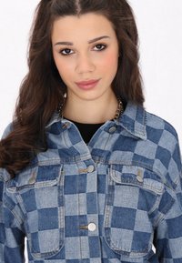 Blå rutigt denimjacka med silverdetaljer, med två bröstfickor, knappstängning och synliga sömmar.