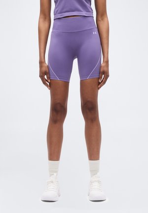 Persoon draagt paars sportshort met hoge taille en bijpassend topje, witte sportsokken en witte sneakers, staand tegen een effen achtergrond.