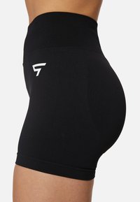 Črne fitnes kratke hlače z visokim pasom, narejene iz raztegljivega materiala, z belim logotipom na strani in oprijetim dizajnom.