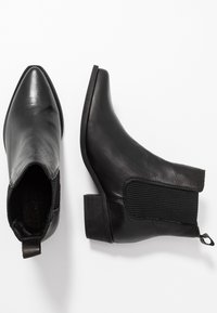 Bottes noires en cuir à bout pointu, avec des panneaux latéraux élastiques et un petit talon carré. Texture lisse avec une languette à l'arrière.