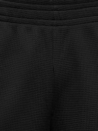 Gros plan sur un tissu gaufré noir texturé en maille gaufrée avec une couture visible et une ceinture, probablement partie d'un vêtement.