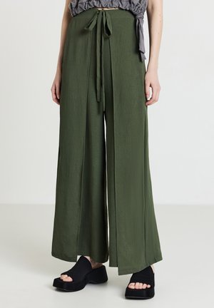 Pantalons larges vert olive avec taille à cordon, fabriqués en tissu léger, présentant un design ample et fluide avec un minimalisme.