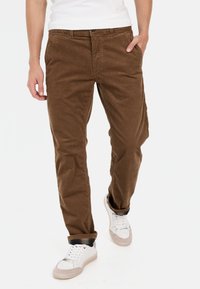 Bruine corduroy broek met een rechte pasvorm, voorzien van frontzakken en een knoopsluiting, gecombineerd met witte sneakers.