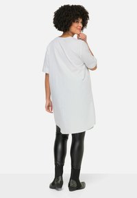 Witte oversized tuniek met korte mouwen en een ronde zoom, gecombineerd met zwarte glanzende leggings en gespschoenen tot de enkels.