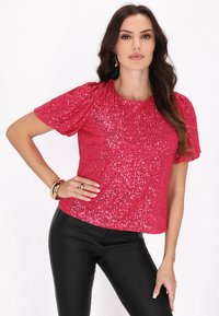 Rövid ujjú, kerek nyakú felső, pink flitterekkel borítva, fekete, testhezálló nadrággal párosítva. Simára csiszolt felület, fényes, tükröződő hatással.