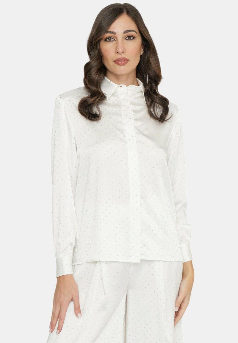 Blusa bianca a maniche lunghe realizzata in tessuto liscio con un delicato motivo a pois, dotata di chiusura con bottoni frontale e un colletto classico.