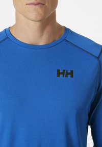 Blauw sportshirt van textuurstof, met een zwart logo op de borst en contrasterende naden langs de schouders.
