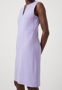 Lawendowa sukienka bez rękawów z dekoltem w serek, uszyta z gładkiego materiału. Posiada boczne kieszenie i czyste linie, wykończona na długości do połowy ud.