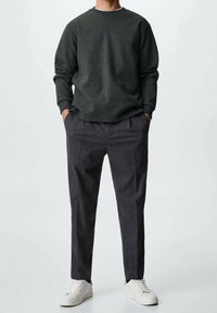 Dunkelgrauer Strickpullover mit rundem Ausschnitt und langen Ärmeln, kombiniert mit anthrazitfarbenen Hosen mit Falten. Weiße Sneaker runden das Outfit ab.