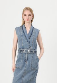 Ujjatlan farmer ruha V-nyakkivágással, világoskék színben, övvel kiemelt derékrésszel és nagy oldalsó zsebekkel.