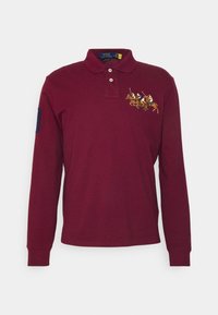 Mörkröd långärmad polo skjorta, tillverkad av bomull, med en krage med två knappar och en broderad design av hästryttare på bröstet.