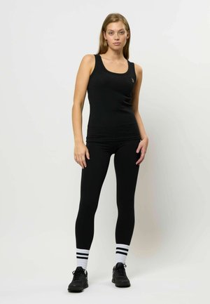 Melnā tvertne, izgatavota no ribota auduma, kombinēta ar melnām legingām, melnām kedām un baltiem zeķēm ar divām melnām svītrām.