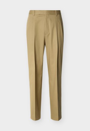 Beige op maat gemaakte broek met taillebandlussen en een voorste plooi, weergegeven tegen een effen lichte achtergrond.