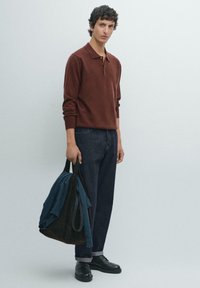 Brązowy sweter polo z dzianiny z kołnierzykiem, niebieskie dżinsy, czarne buty oraz ciemna torba z turkusową koszulą w środku. Prosty design, casualowy krój.