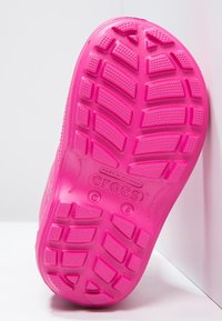 Semelle en caoutchouc rose avec un design de bande de roulement à motifs. Présente le logo "CROCS" et un texte moulé pour la taille et l'origine. Texture lisse.
