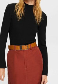 Schwarzes, geripptes Langarmoberteil, das mit einem rostfarbenen Rock kombiniert ist. Der Gürtel ist beige mit einer metallischen Schnalle, die die Taille betont.