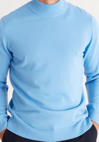 Ljusblå stickad tröja med hög ribbad krage och ribbade ärmslut, med en mjuk textur och figursydd design.