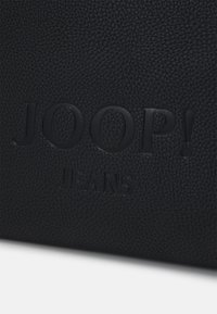 Črn usnjen nahrbtnik s strukturo, ki vsebuje embosirani logotip "JOOP! JEANS". Površina ima kamenčkov končni videz z mat površino.