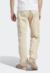 Pantalones cargo de color beige claro con bolsillos laterales y un ajuste relajado, confeccionados en tela texturizada. Combinados con zapatillas deportivas de tonos neutros.