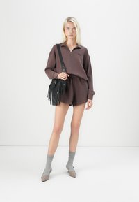 Brun zip-up genser med ribbet tekstur, kombinert med matchende shorts og en svart fransete håndveske. Lys grå ankelstrømper og spisse heler.