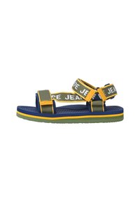 Sandal s plavom, zelenom i žutom shemom boja. Ima podesive platnene trake s natpisom "JEANS" i teksturiranu gumenu potplatu.