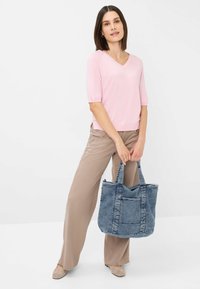 Lyserød kortærmet V-hals sweater, beige vide bukser og blå denim tote taske med dobbelte håndtag og forlommer.